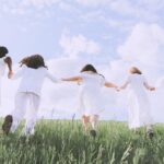 cinco mulheres vestidas de branco de mãos dadas correndo num campo